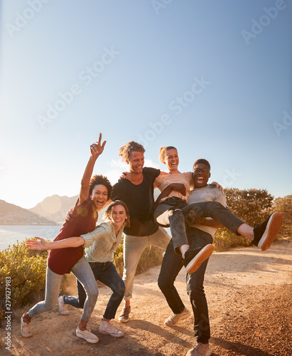 Five millennial friends on a road trip have fun posing for photos on a coastal path, full length photo