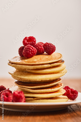 selective focus of tasty pancakes with raspberries on plate isolated on grey