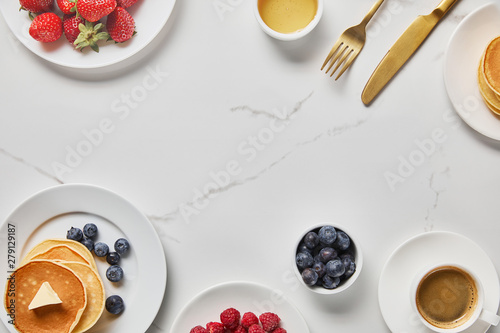top view of tasty breakfast with pancakes, honey, different kinds of berries and cup of coffee