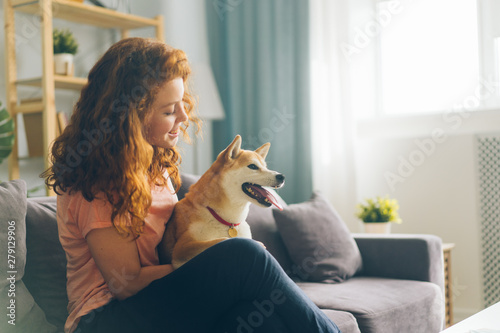 Pretty redhead woman is hugging cute doggy sitting on couch in apartment smiling enjoying beautiful day with beloved animal. People and pets concept. photo