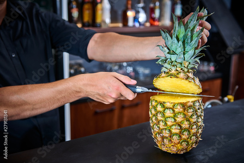 Barkeepr cutting pineapple on the counter bar in a pub with blurry background