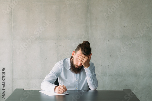 Resignation notice. Tired bearded man writing formal letter. Gray wall background. Copy space.