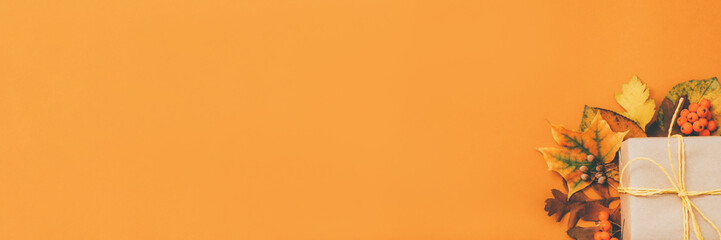 Autumn holiday composition. Orange background with cropped beige paper gift box and foliage. Copy space.