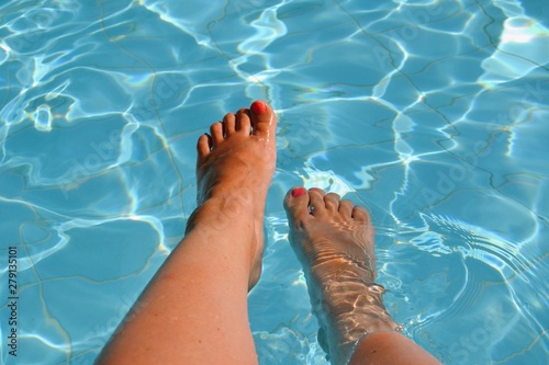 Female feet, legs in swimming pool. All inclusive. Summer holidays, vacation, relax concept. Red nails, suntanned skin, turquoise water.  © PaulSat