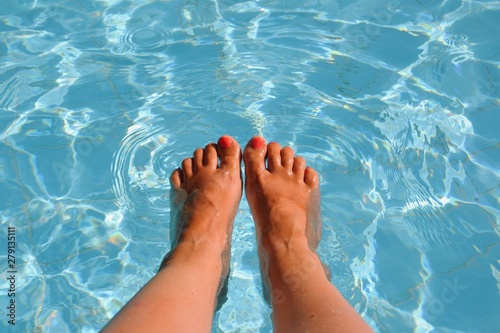 Female feet, legs in swimming pool. All inclusive. Summer holidays, vacation, relax concept. Red nails, suntanned skin, turquoise water. 