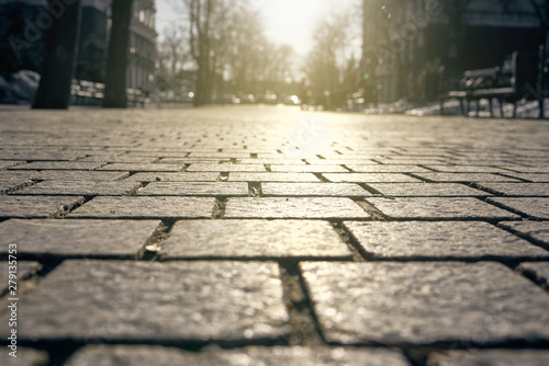 Paving tiles illuminated by sunlight background. Paving slabs close-up on the background of streets, trees and sky in blur.
