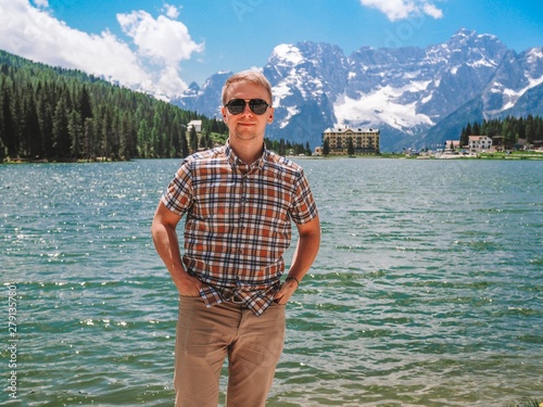 A young blond man in a plaid shirt against the backdrop of lake Mizurina in the Dolomites mountains, Italy. Amazing view of the lake. photo