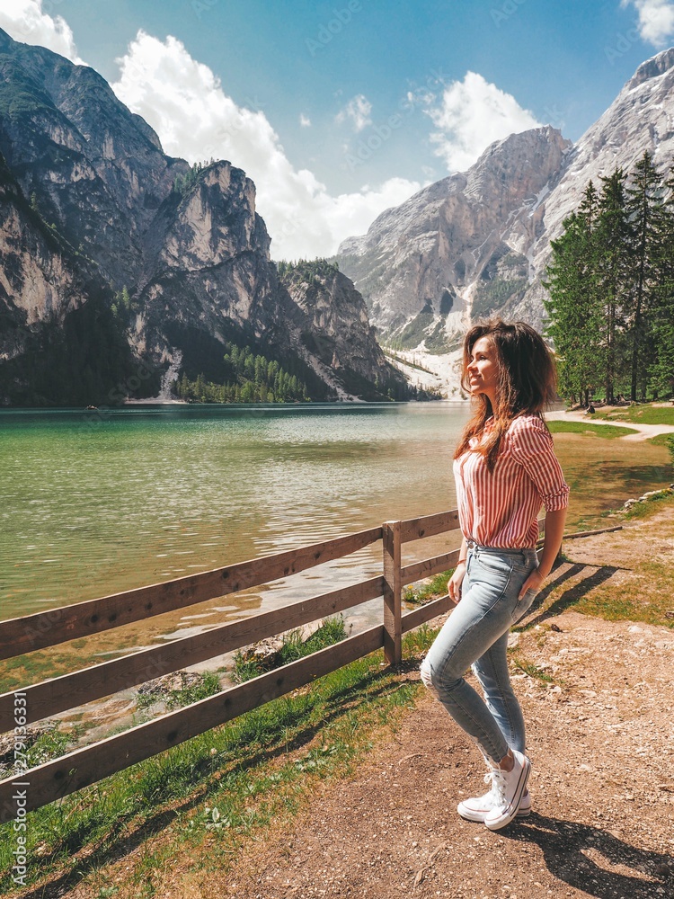 Naklejka premium Girl with long hair in striped shirt in the background of Lake Lago di Braies in the Dolomites, South Tyrol, Italy. Pier with romantic old wooden rowing boats on the lake. Amazing view of lake Lago di