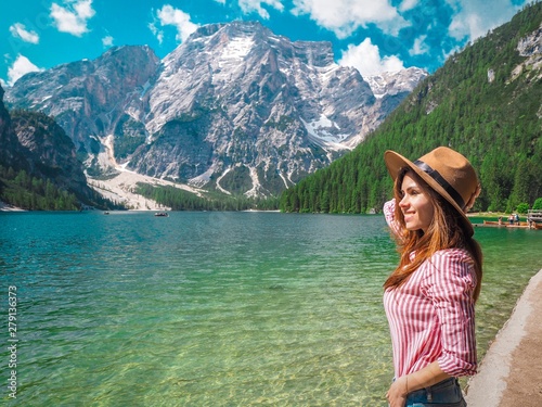 The girl with long hair wearing a wide-brimmed hat and a shirt striped on a background of Lake Lago di Braies in the Dolomites, South Tyrol, Italy. Pier with romantic old wooden rowing boats 