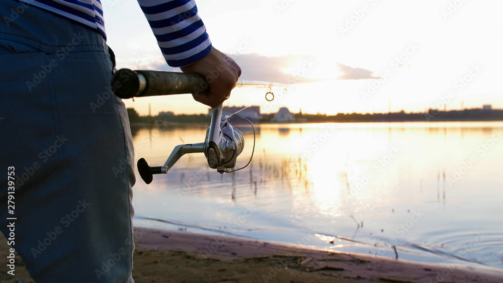 A man in striped shirts with fishing rods staying on the riverside at sunset