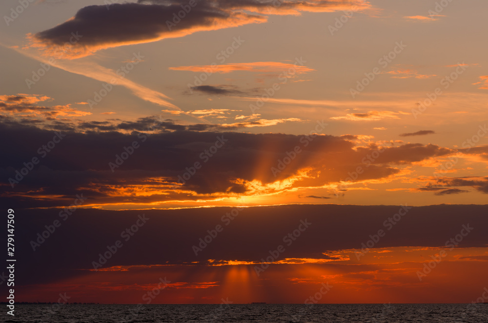 Beautiful sunset with cloudy sky over the sea, focus on waves and horizon. The sun sets and the rays illuminate the clouds. Nature dramatic colorful landscape. Scenery view of the sundown and calm sea