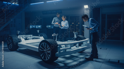 Diverse Automobile Engineers Talking while Working on Electric Car Platform Chassis Prototype. In Automotive Innovation Facility Concept Vehicle Frame Includes Tires, Suspension, Engine and Battery © Gorodenkoff
