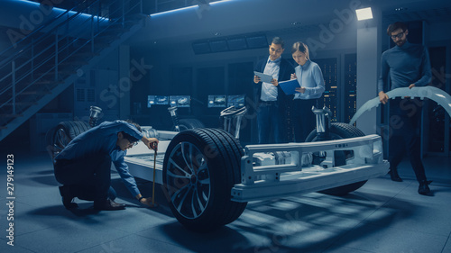 Team of Automotive Engineers Working on Electric Car Platform Chassis, Taking Measures, working with 3D CAD Software, Analysing Efficiency. Vehicle Frame with Wheels, Engine and Battery. © Gorodenkoff