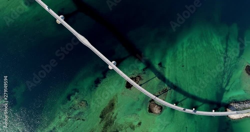 Aerial top-down static shot of tourist cars and camper crossing beautiful road bridge in amazing fjord scenery with green and blue water shades.