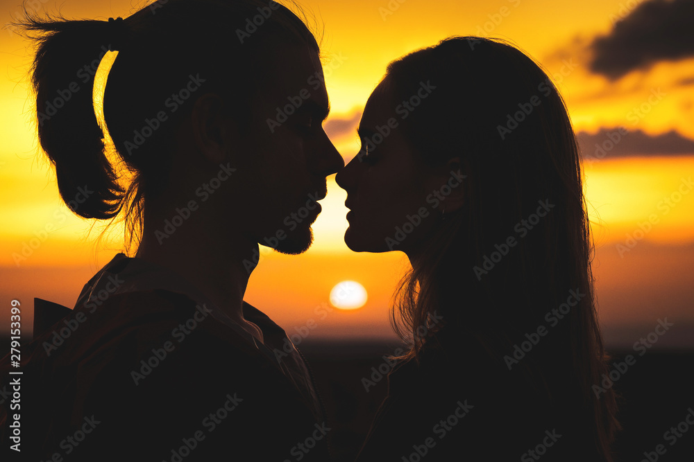 Close-up of the silhouettes of a young millenial couple in love getting ready to kiss with a man and girl against the sunset golden sky. They look at each other. Young family