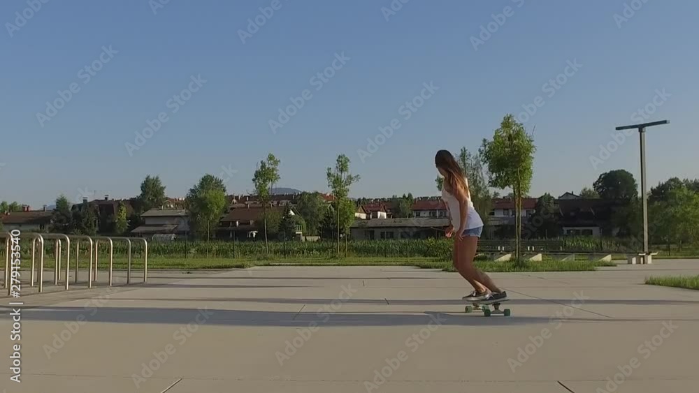 SLOW MOTION Close-up of young cute girl with long brown hair skateboarding next to a city park, shot from behind SLOW MOTION Close-up of young cute girl with long brown hair skateboarding next to a city park, shot from behind