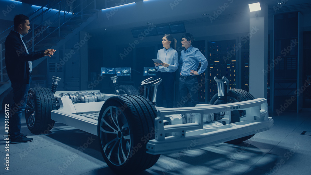 Automobile Design Engineers Talking while Working on Electric Car Chassis Prototype. In Automotive Innovation Facility Concept Vehicle Frame Includes Tires, Suspension, Engine and Battery Automobile Design Engineers Talking while Working on Electric Car Chassis Prototype. In Automotive Innovation Facility Concept Vehicle Frame Includes Tires, Suspension, Engine and Battery