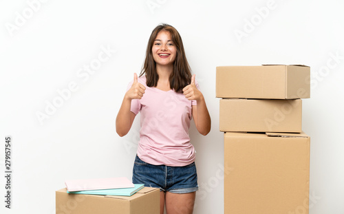 Young girl moving in new home among boxes giving a thumbs up gesture