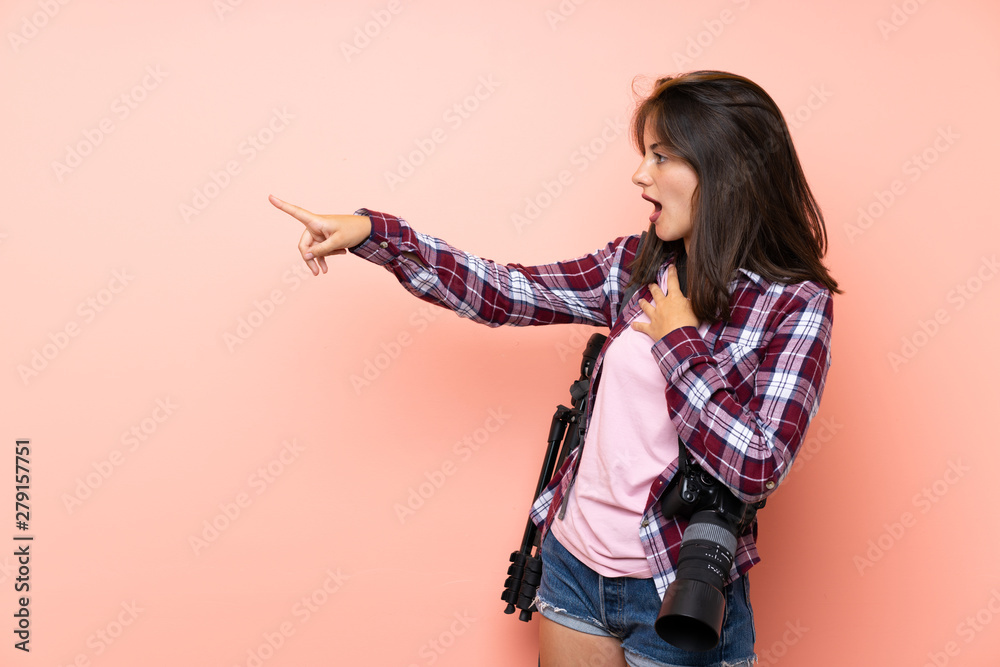 Young photographer girl over isolated pink background pointing finger to the side