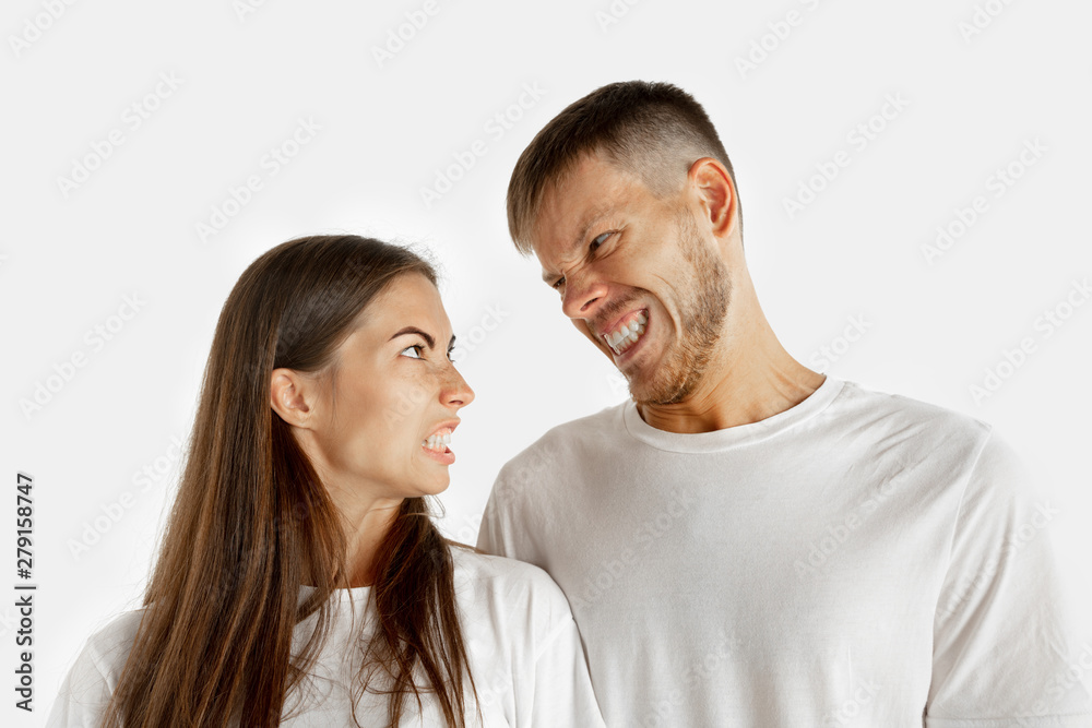 Beautiful young couple's portrait isolated on white studio background. Facial expression, human emotions, advertising concept. Man and woman standing, looking at each other with an angry. Beautiful young couple's portrait isolated on white studio background. Facial expression, human emotions, advertising concept. Man and woman standing, looking at each other with an angry.