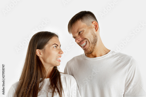 Beautiful young couple's portrait isolated on white studio background. Facial expression, human emotions, advertising concept. Man and woman standing, looking at each other with an angry.