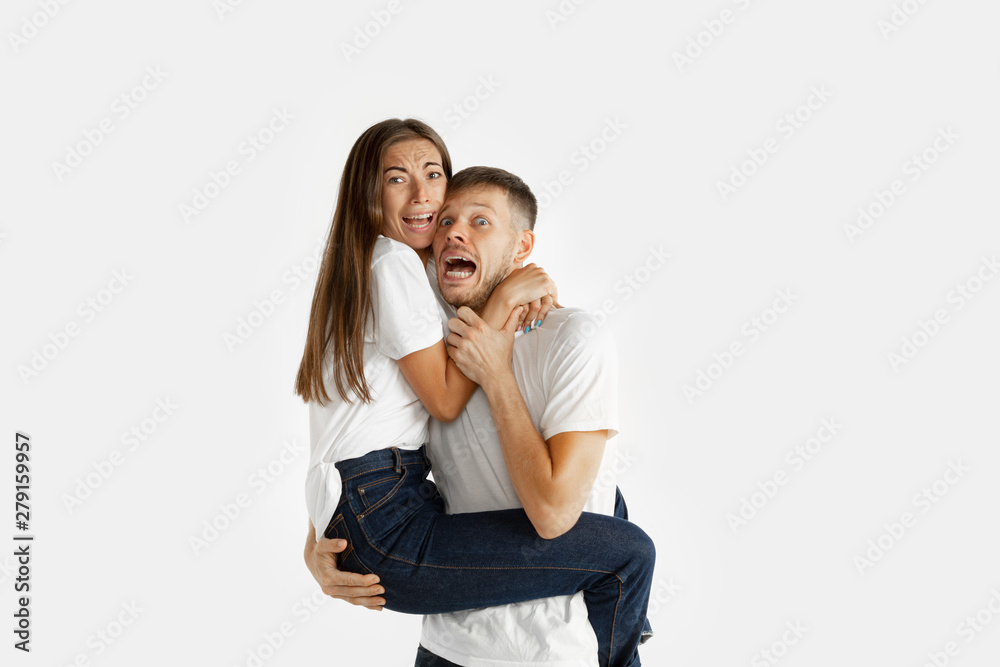 Beautiful young couple's portrait isolated on white studio background. Facial expression, human emotions, advertising, relation concept. Man and woman holding each other, look scared, screaming. Beautiful young couple's portrait isolated on white studio background. Facial expression, human emotions, advertising, relation concept. Man and woman holding each other, look scared, screaming.