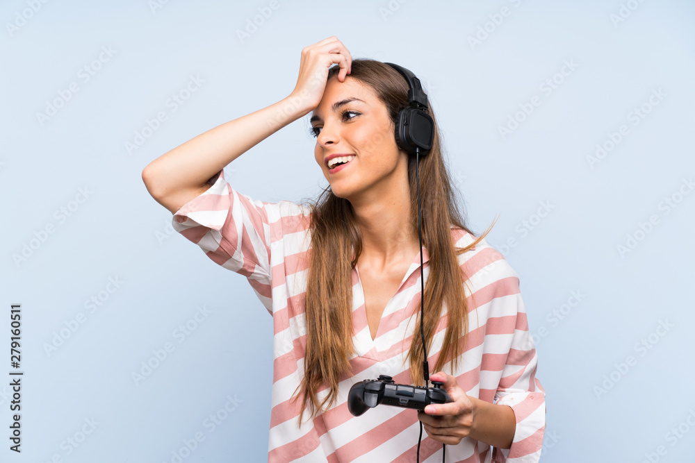 Young woman playing with a video game controller over isolated blue wall has realized something and intending the solution Young woman playing with a video game controller over isolated blue wall has realized something and intending the solution