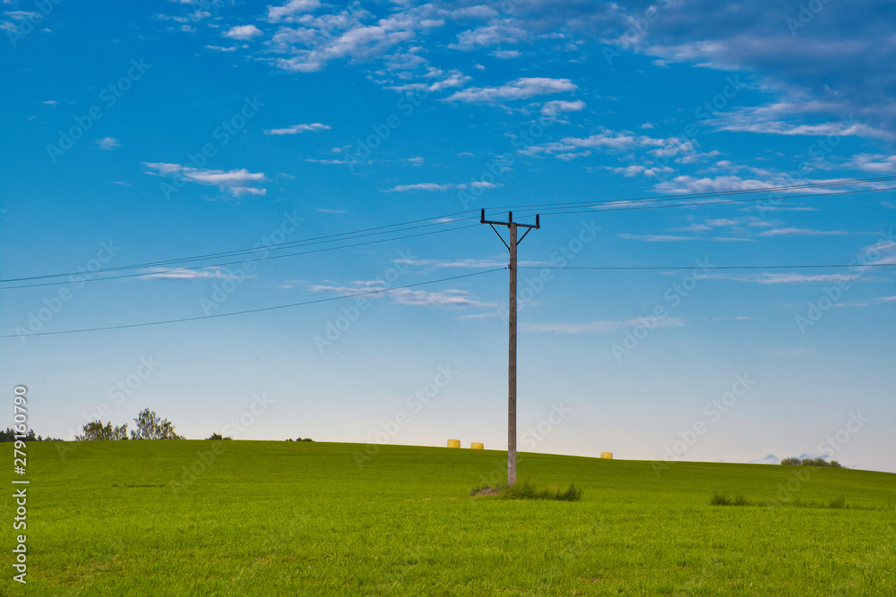 Obraz premium Electric pole on a green field with hay bales in the background