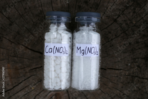 Two glass jars with white crystalline substances: calcium nitrate and magnesium nitrate are the most effective nitrogen fertilizers. On the surface of dark wood. photo