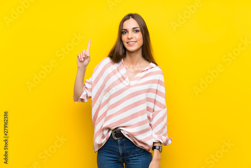 Young woman over isolated yellow background showing and lifting a finger in sign of the best