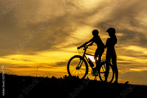 Silhouette biker lovely family at sunset over the ocean. Mom and daughter bicycling chill and relax at the beach. Lifestyle Concept.