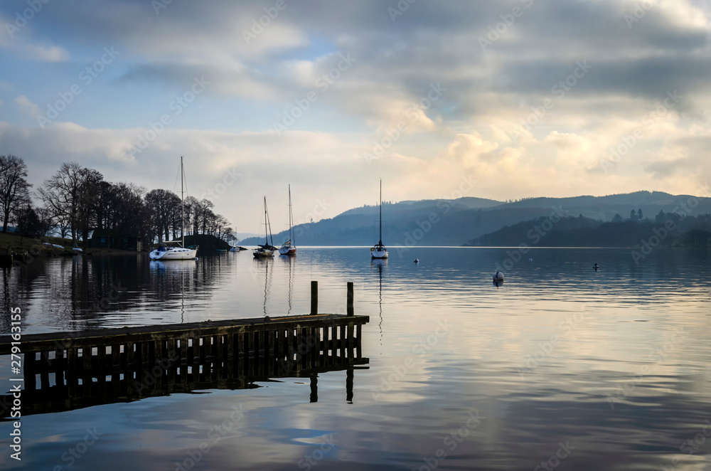 A still quiet peaceful evening at Lake Windermere showing a pier boats and a calm lake.
