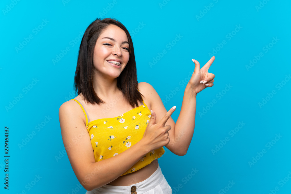 Young Mexican woman over isolated blue background pointing finger to the side