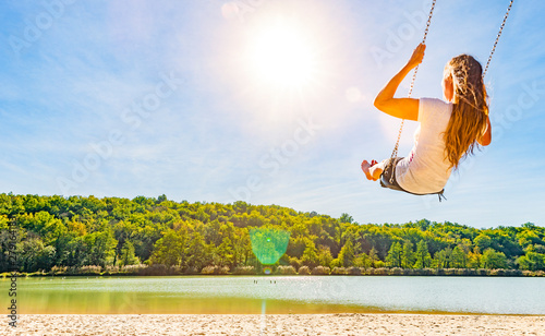 Frau auf einer Schaukel an einem See mit Sandstrand