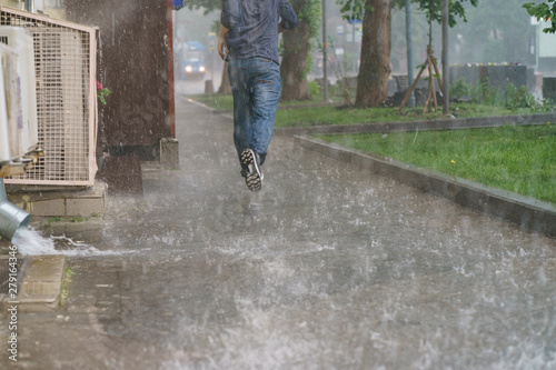 Raining day in the city at summer time. A wet young man running in the rain. Texture of strong, fresh and powerful water drops and sprays. Puddle with ripple on Moscow road. Power, energy in nature