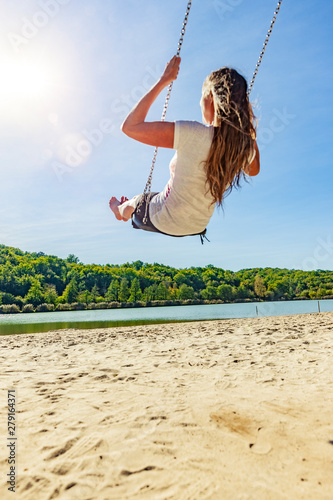 Frau auf einer Schaukel an einem See mit Sandstrand