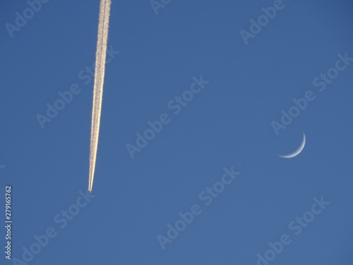 estela blanca de avion reactor sobre cielo azul con luna creciente en blanco photo