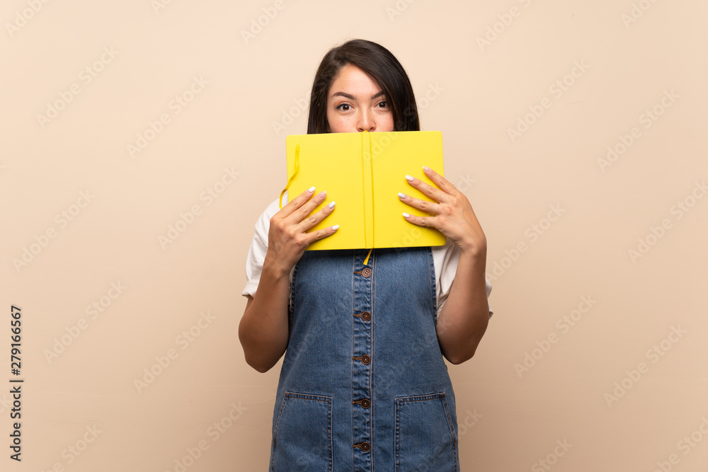 Young Mexican woman over isolated background holding and reading a book Young Mexican woman over isolated background holding and reading a book