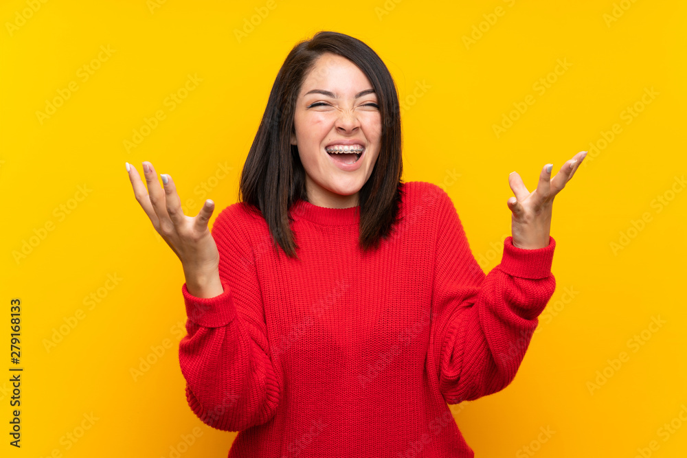 Young Mexican woman with red sweater over yellow wall unhappy and frustrated with something Young Mexican woman with red sweater over yellow wall unhappy and frustrated with something