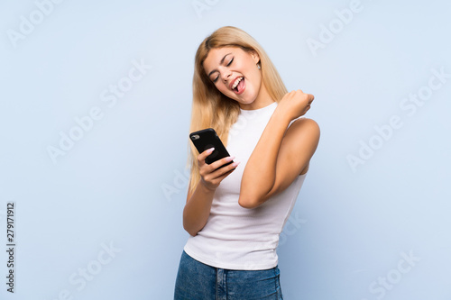 Teenager girl over isolated blue background points finger at you while smiling