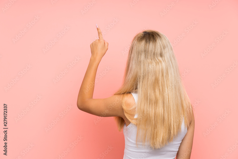 Teenager girl over isolated pink background pointing back with the index finger Teenager girl over isolated pink background pointing back with the index finger