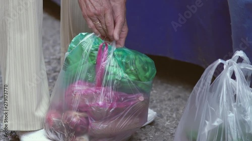 Elderly woman's hands tying various plastic carrying bags filled with vegetables together at a farmers street market in slow motion.