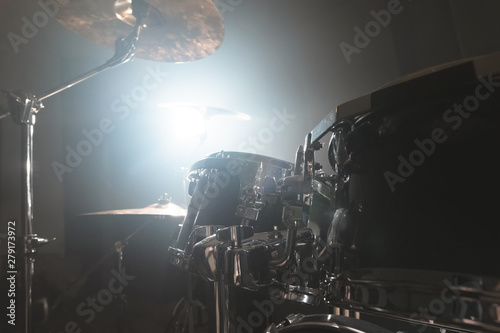 Close-up black drums A modern drum set prepared for playing in a dark rehearsal room on stage with a bright spotlight. The concept of percussion musical instruments