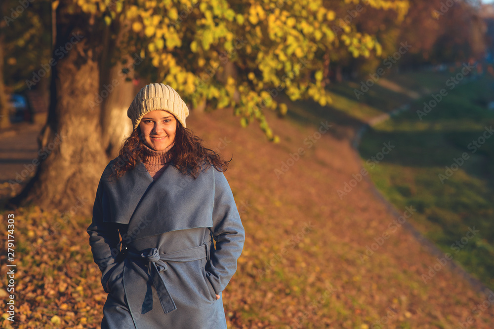 Autumn woman outdoors portrait. Young woman dressed in blue coat and knitted hat walks in autumn park. People, lifestyle and autumn concept. Beautiful autumn sunny day. Copy space. Autumn woman outdoors portrait. Young woman dressed in blue coat and knitted hat walks in autumn park. People, lifestyle and autumn concept. Beautiful autumn sunny day. Copy space.