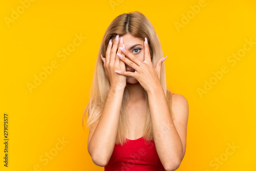 Teenager girl over isolated yellow background covering eyes and looking through fingers © luismolinero
