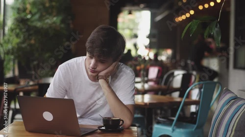 Bored Young man surfing website and chatting, freelancer and blogger working as a graphic designer indoor, modern working place sitting in cafe. Open laptop in restaurant.