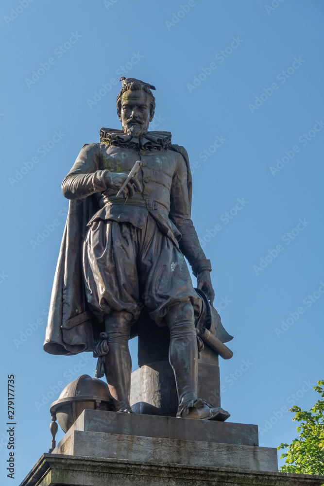 Obraz premium Bruges, Flanders, Belgium - June 17, 2019: Closeup of Simon Stevin statue under blue sky. Some green foliage. Pigeon on his head.