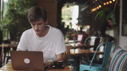 Young man finish work, freelancer and blogger working as a graphic designer indoor, modern working place sitting in cafe. Open laptop in restaurant.