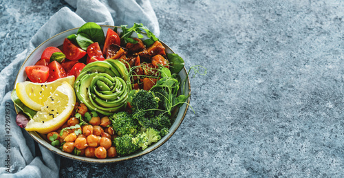 Buddha bowl salad with baked sweet potatoes, chickpeas, broccoli, tomatoes, greens, avocado, pea sprouts on light blue background with napkin. Healthy vegan food, clean eating, dieting, top view