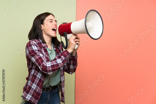 Young woman over isolated colorful wall shouting through a megaphone